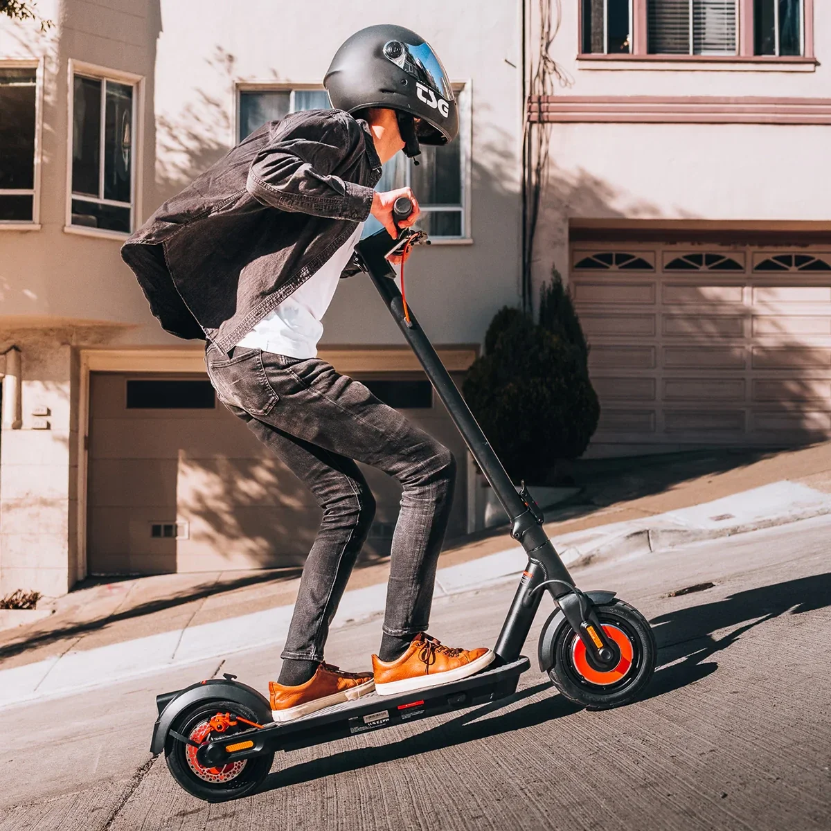 A rider wearing a helmet riding a sleek electric scooter uphill on a sunny day.