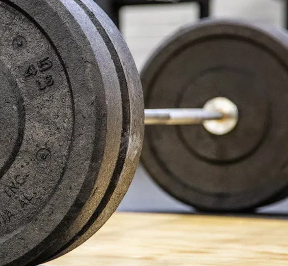 Close-up of a barbell with weight plates resting on a gym floor, ideal for strength training and weightlifting. Visit waiteandsea.com.au