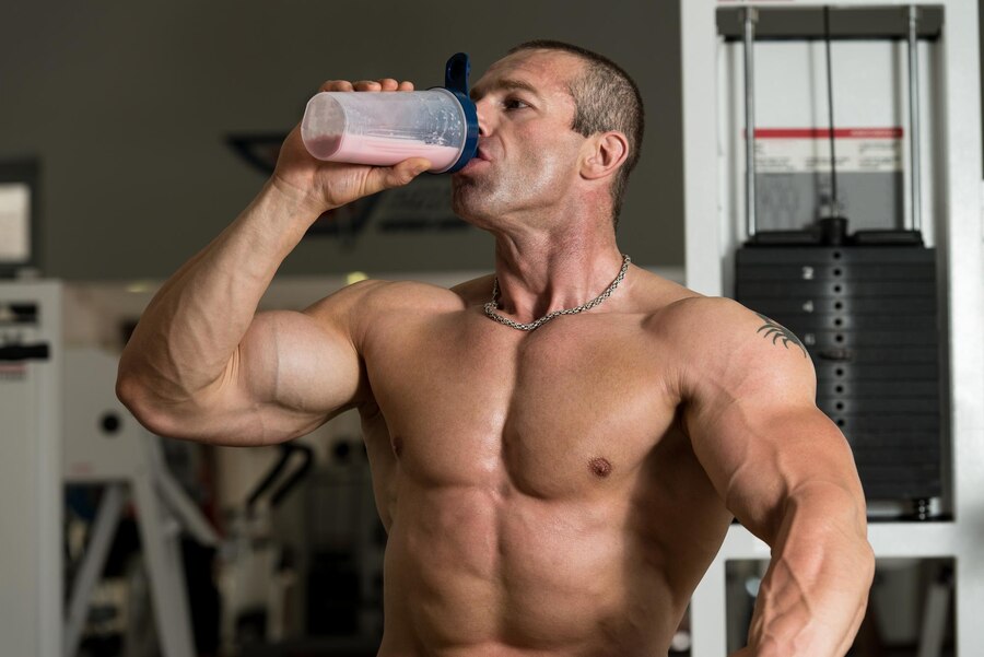 A muscular man drinking a protein shake in a gym, promoting health and fitness. Visit www.waiteandsea.com.au for fitness tips and supplements.