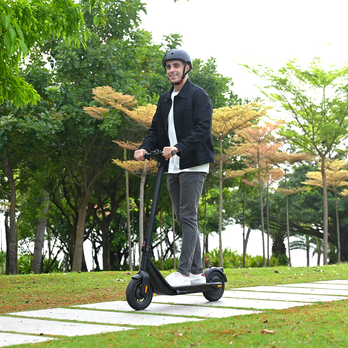 A man riding an InMotion Air electric scooter through a scenic park pathway surrounded by lush green trees.