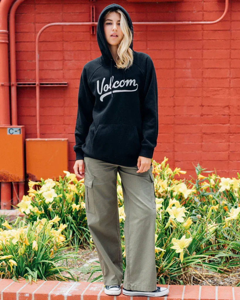A young woman walking confidently in a black Volcom hoodie paired with green cargo pants, perfect for a casual and functional health and fitness-inspired look. Find it at www.waiteandsea.com.au.