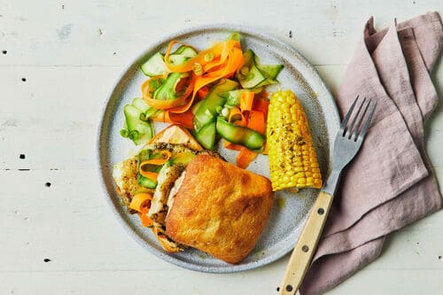 Crispy fish served in a toasted bap with smoky aioli, corn on the cob, and a fresh carrot-cucumber salad.