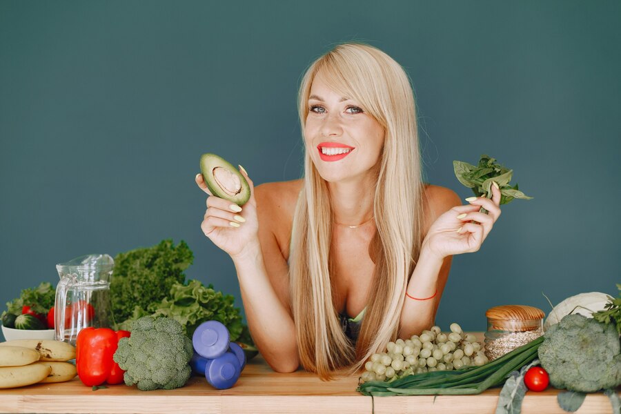 Smiling woman surrounded by fresh fruits, vegetables, and fitness accessories, promoting healthy eating and an active lifestyle. Learn more about health and fitness at www.waiteandsea.com.au.