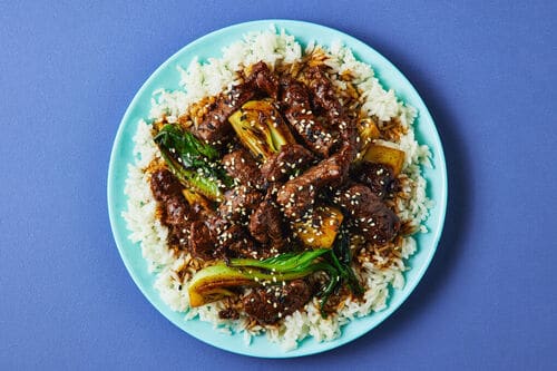 A colourful plate of glazed beef stir-fry with bok choy, served over steamed rice and topped with sesame seeds.