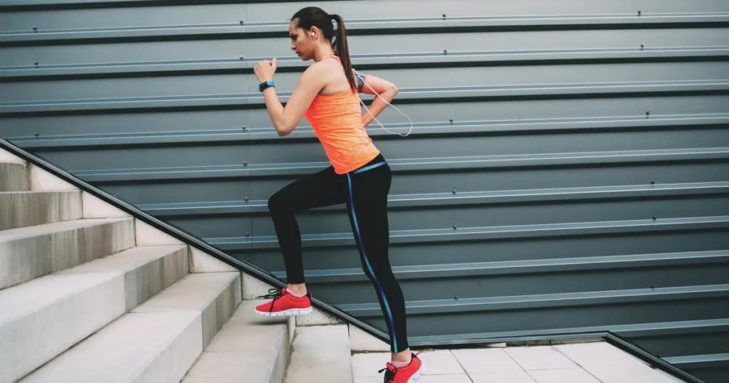 A woman in athletic wear running up stairs outdoors, highlighting health and fitness through cardio training.