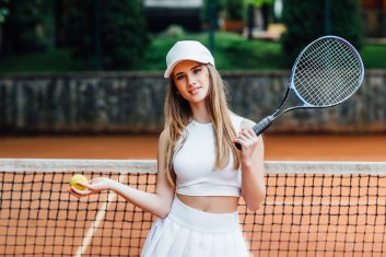 Young female tennis player on a clay court, holding a racket and tennis ball, representing health and fitness.